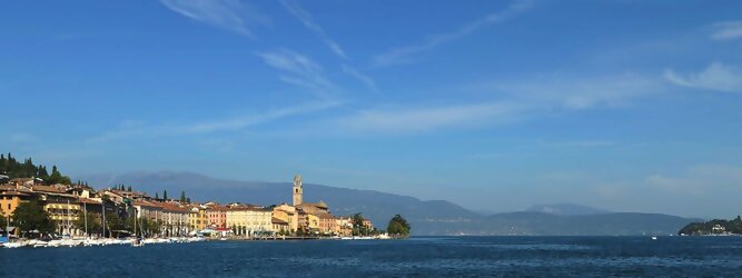 GranCanariaFerienhaus beliebte Urlaubsziele am Gardasee -  Mit einer Fläche von 370 km² ist der Gardasee der größte See Italiens. Es liegt am Fuße der Alpen und erstreckt sich über drei Staaten: Lombardei, Venetien und Trentino. Die maximale Tiefe des Sees beträgt 346 m, er hat eine längliche Form und sein nördliches Ende ist sehr schmal. Dort ist der See von den Bergen der Gruppo di Baldo umgeben. Du trittst aus deinem gemütlichen Hotelzimmer und es begrüßt dich die warme italienische Sonne. Du blickst auf den atemberaubenden Gardasee, der in zahlreichen Blautönen schimmert - von tiefem Dunkelblau bis zu funkelndem Türkis. Majestätische Berge umgeben dich, während die Brise sanft deine Haut streichelt und der Duft von blühenden Zitronenbäumen deine Nase kitzelt. Du schlenderst die malerischen, engen Gassen entlang, vorbei an farbenfrohen, blumengeschmückten Häusern. Vereinzelt unterbricht das fröhliche Lachen der Einheimischen die friedvolle Stille. Du fühlst dich wie in einem Traum, der nicht enden will. Jeder Schritt führt dich zu neuen Entdeckungen und Abenteuern. Du probierst die köstliche italienische Küche mit ihren frischen Zutaten und verführerischen Aromen. Die Sonne geht langsam unter und taucht den Himmel in ein leuchtendes Orange-rot - ein spektakulärer Anblick.